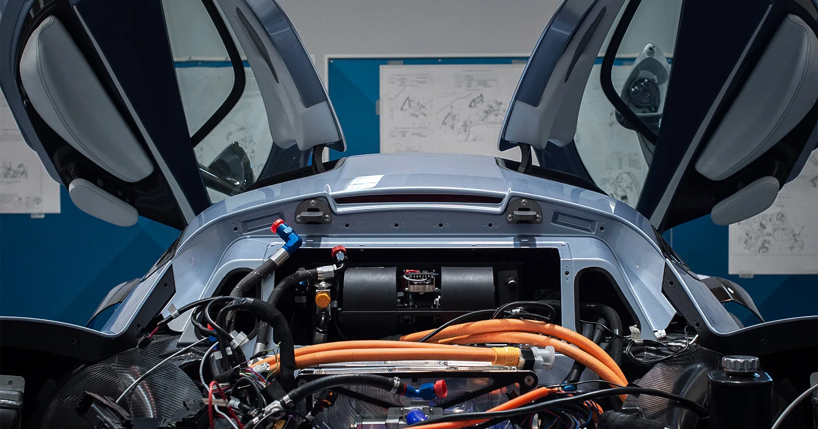 Exposed engine bay of a sports car with gullwing doors open and prominent orange wiring